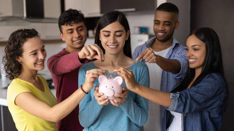 several people standing around a piggybank, reaching over to put in change