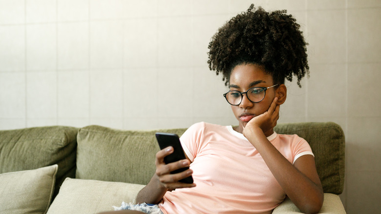 person sitting on couch, frowning at smartphone