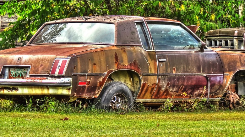 Oldsmobile Cutlass rusting in a grass lot