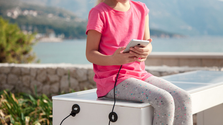 person charging smartphone on USB bench