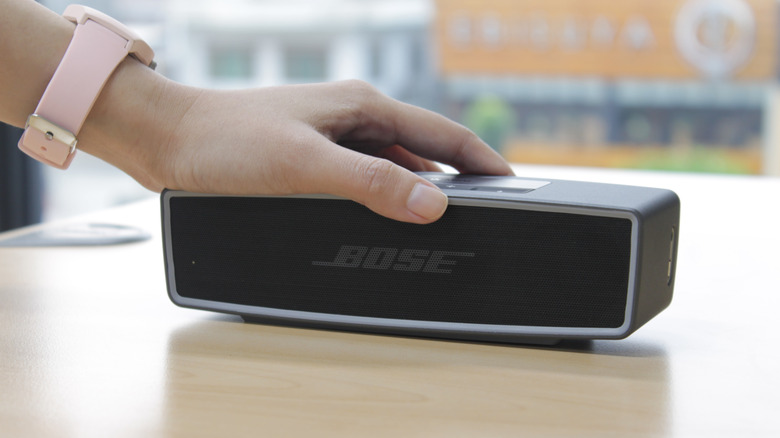 Hand touching a BOSE speaker on a wooden table