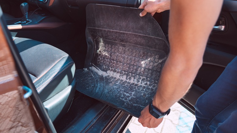 holding a dirty car floor mat