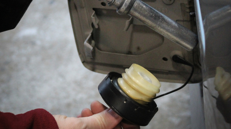 close-up of gasoline nozzle and man holding a fuel cap