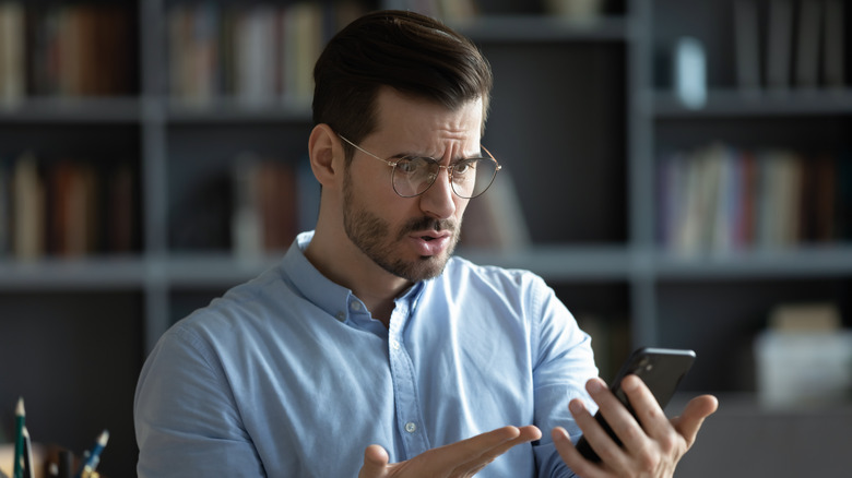 A worried man wearing glasses looking at his iPhone