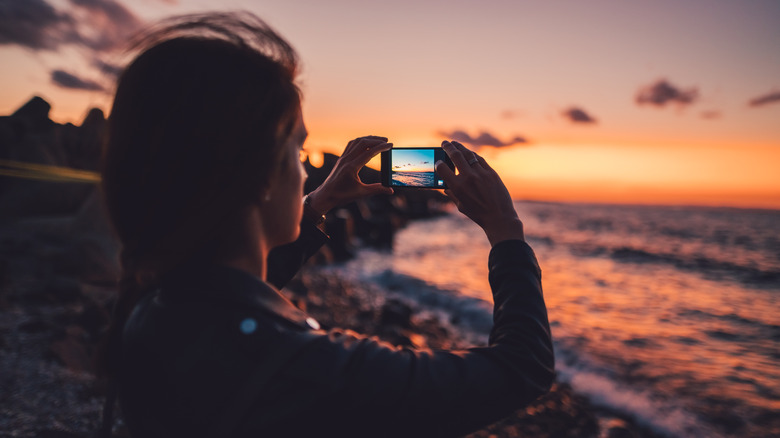 person taking picture of ocean sunset