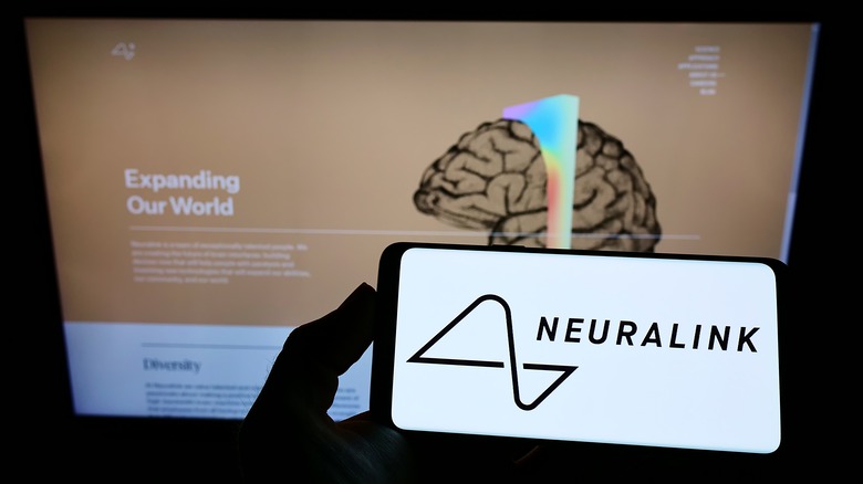person holding smartphone with Neuralink logo on the screen