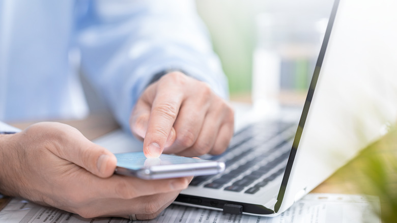 person using smartphone by laptop