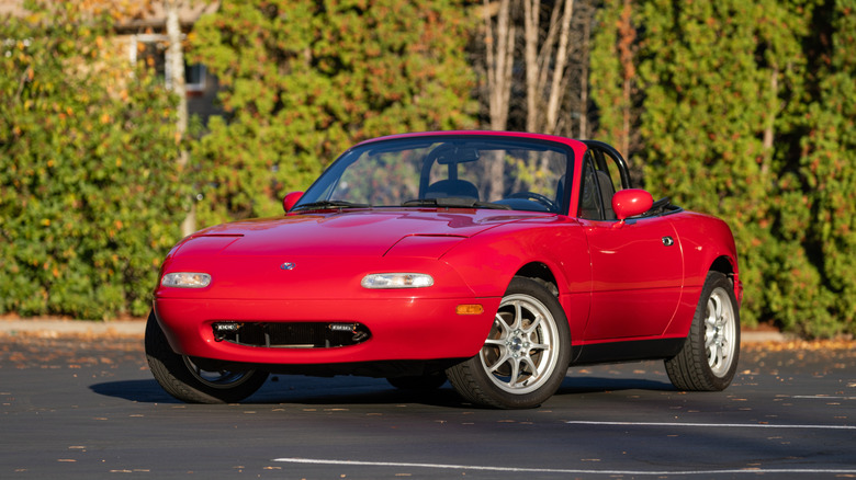 An NA Mazda Miata in red with the roof down, front 3/4 view, aftermarket wheels