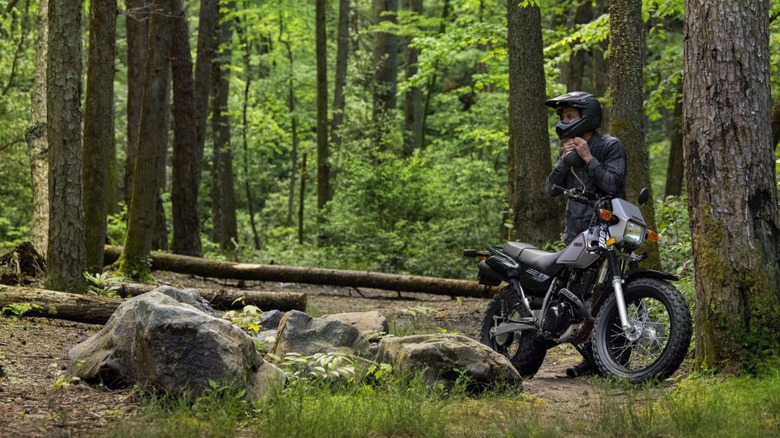 Person mounting Yamaha TW200 in forest