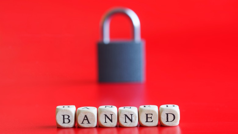 The word "Banned" written in all caps on cubes with a closed padlock in the background, both on a bright red background.