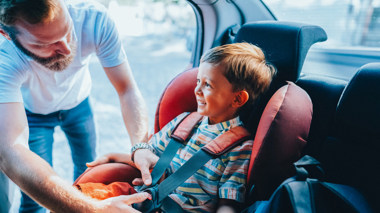 A father straps in a smiling boy into his car seat