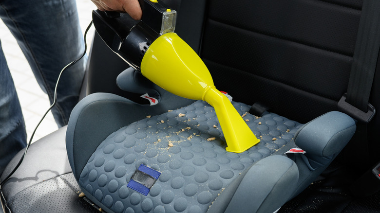 A person vacuums a booster seat in a car