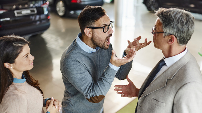 Frustrated man and his wife are talking to an agent in a car parking lot